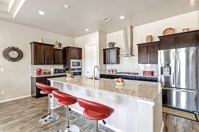 kitchen featuring wall chimney range hood, a sink, stainless steel appliances, wood finished floors, and visible vents
