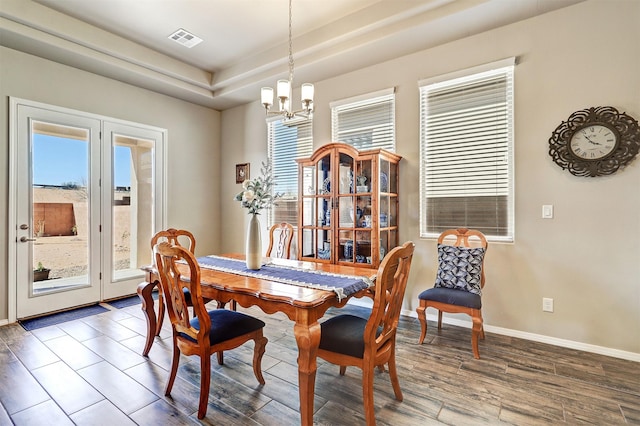 dining space with an inviting chandelier, baseboards, wood finished floors, a tray ceiling, and visible vents