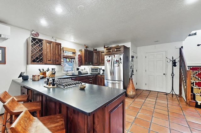 kitchen with dark countertops, appliances with stainless steel finishes, a breakfast bar, a textured ceiling, and a peninsula