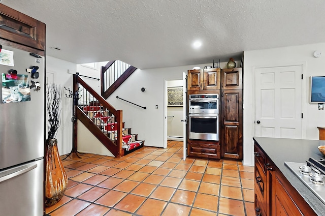 kitchen with a textured ceiling, light tile patterned flooring, dark countertops, and stainless steel appliances