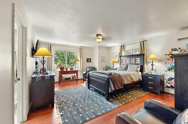 bedroom with a baseboard radiator, an AC wall unit, hardwood / wood-style flooring, and a textured ceiling