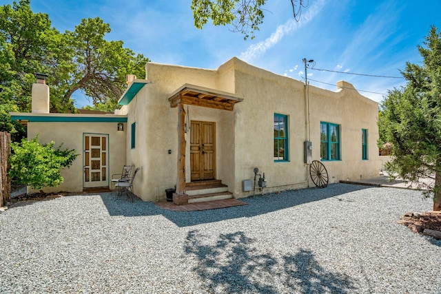 pueblo-style home featuring stucco siding and a chimney