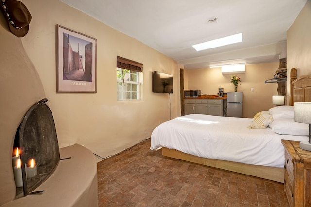 bedroom featuring brick floor and freestanding refrigerator