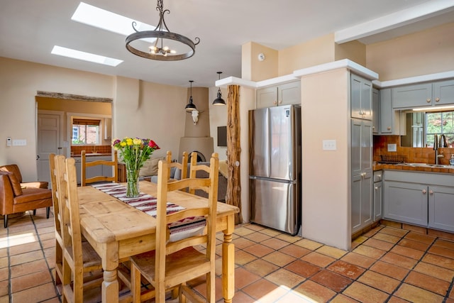 kitchen with freestanding refrigerator, gray cabinets, a sink, backsplash, and a notable chandelier