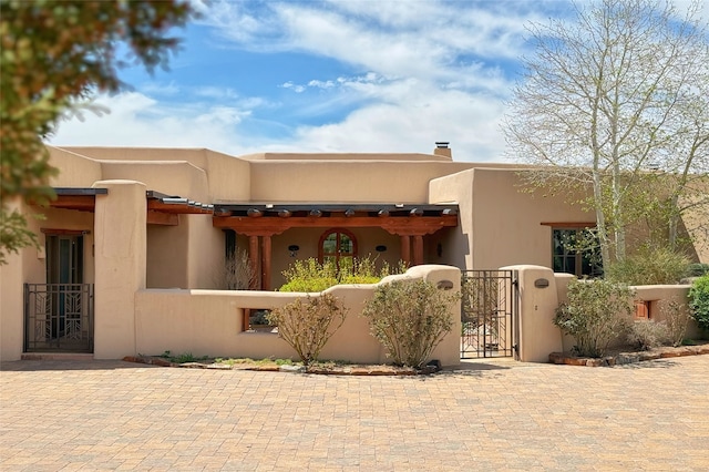 pueblo revival-style home featuring stucco siding, a gate, and fence