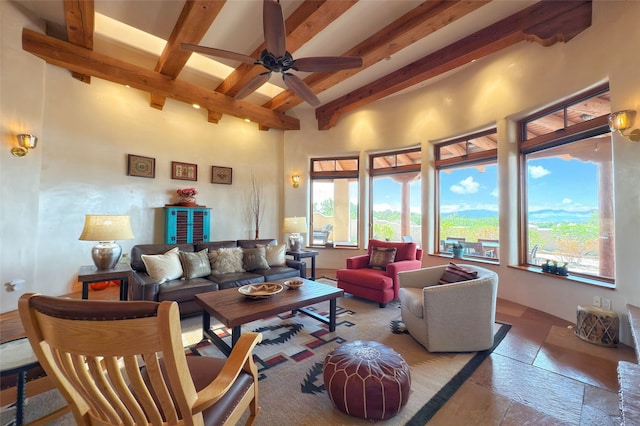 living area featuring a ceiling fan, beam ceiling, and stone tile floors