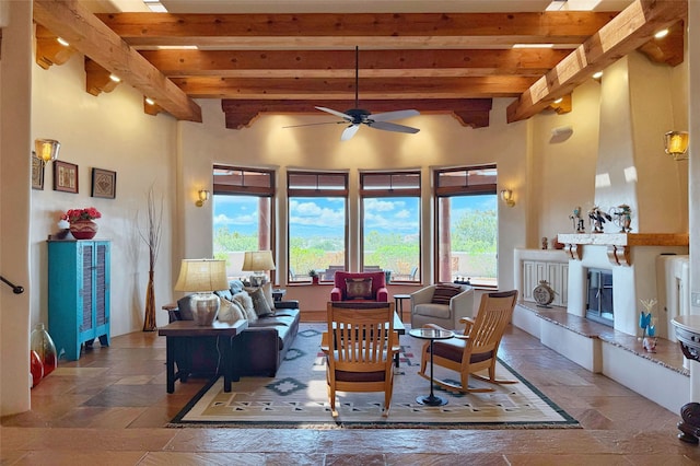 living room featuring a fireplace, beam ceiling, a ceiling fan, and stone tile flooring