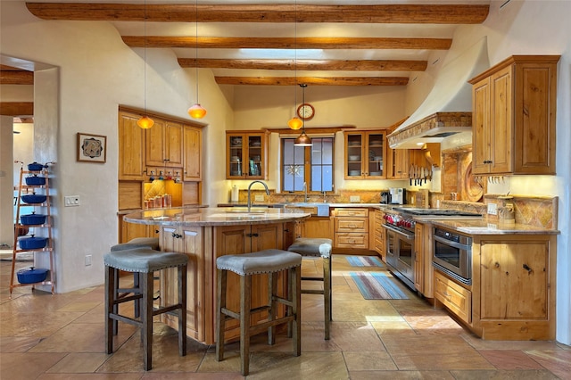 kitchen with a kitchen island with sink, tasteful backsplash, light stone countertops, a sink, and beamed ceiling
