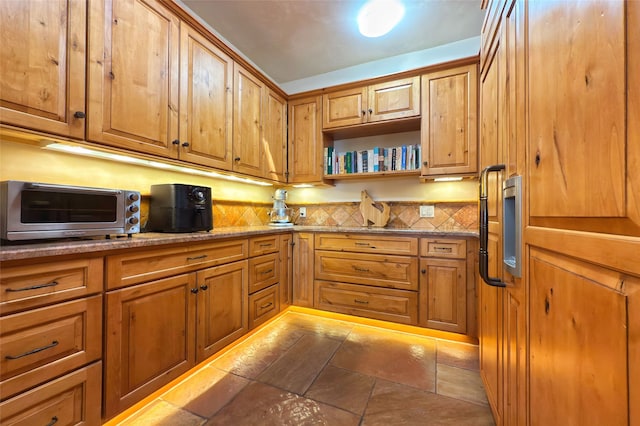 kitchen featuring decorative backsplash, light stone counters, brown cabinetry, and a toaster