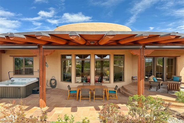back of property with a hot tub, a patio area, and stucco siding