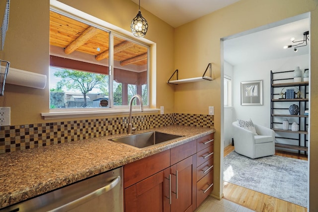 kitchen with a sink, light wood-style flooring, backsplash, stainless steel dishwasher, and pendant lighting