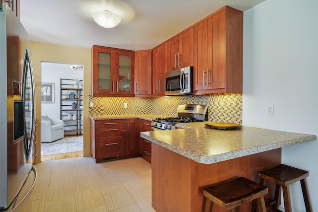 kitchen featuring appliances with stainless steel finishes, a breakfast bar, a peninsula, backsplash, and glass insert cabinets