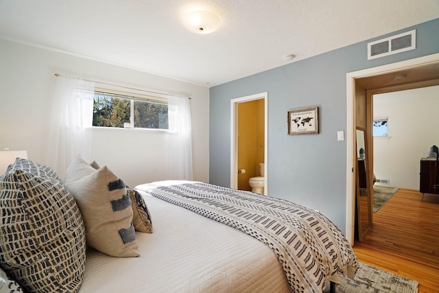 bedroom featuring connected bathroom, wood finished floors, and visible vents