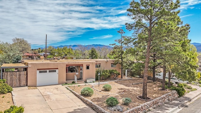 pueblo-style home featuring an attached garage, a mountain view, stucco siding, and concrete driveway