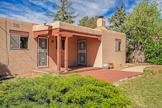 back of house with stucco siding and a chimney