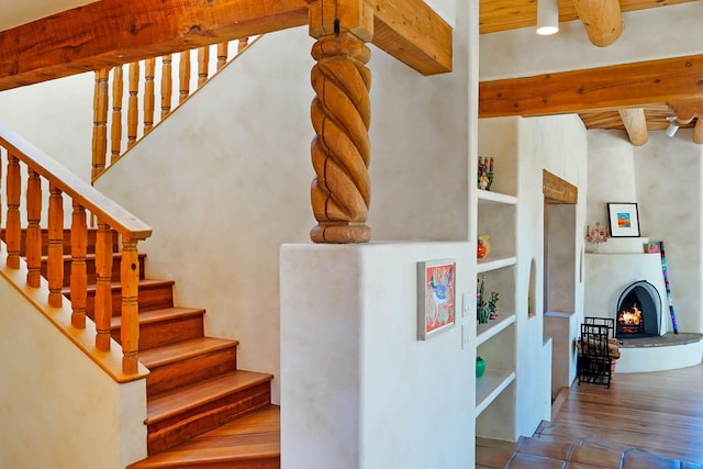 stairway featuring built in features, wood finished floors, beamed ceiling, a high ceiling, and a warm lit fireplace