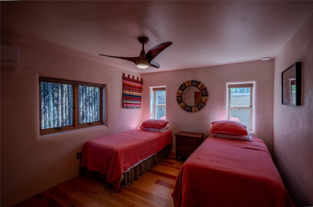 bedroom with a wall mounted air conditioner, light wood finished floors, and ceiling fan