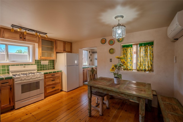 kitchen featuring white appliances, light wood-style floors, a wall mounted air conditioner, tile counters, and backsplash