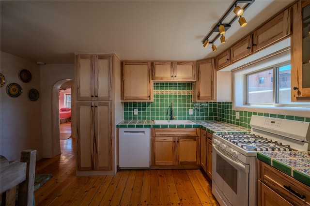 kitchen featuring a sink, arched walkways, tile countertops, and white appliances