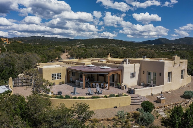 rear view of house with a mountain view, stucco siding, a chimney, and a patio