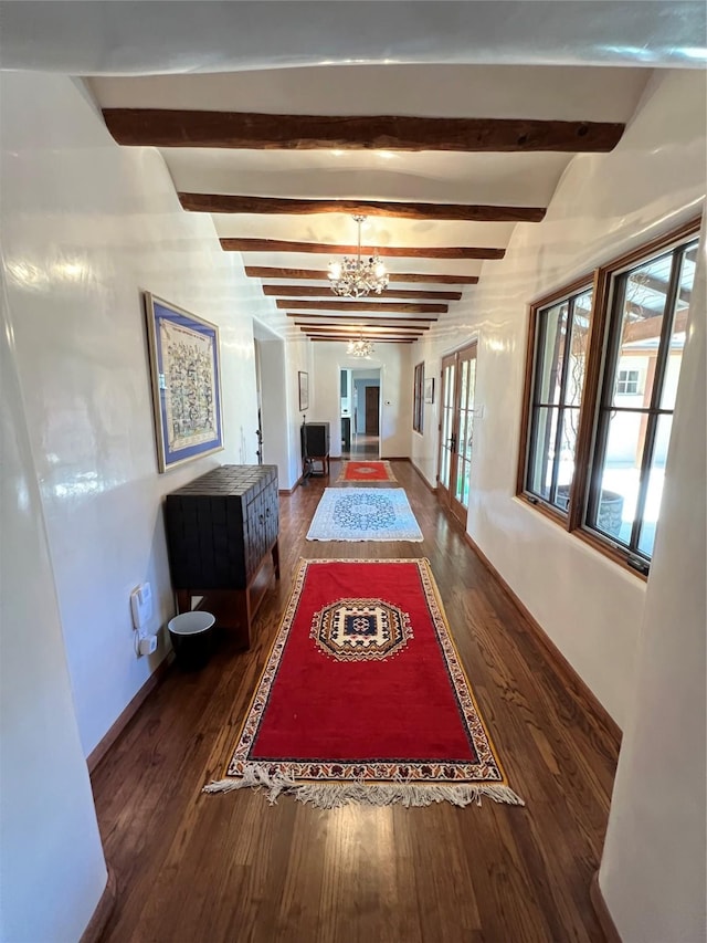 corridor with baseboards, an inviting chandelier, beam ceiling, and dark wood-type flooring