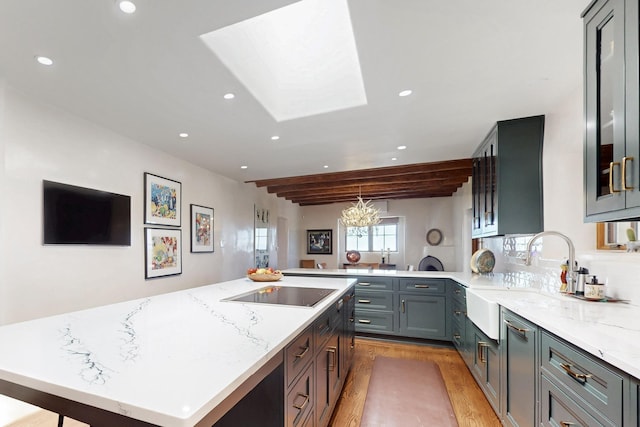 kitchen featuring a kitchen island, light wood-type flooring, black electric cooktop, a sink, and a notable chandelier