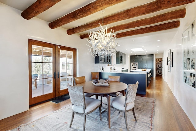 dining area featuring an inviting chandelier, light wood finished floors, french doors, and beamed ceiling