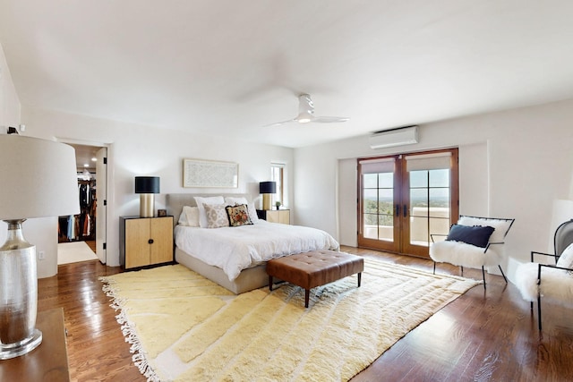 bedroom with wood finished floors, an AC wall unit, access to outside, french doors, and a ceiling fan