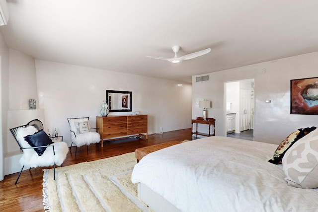 bedroom featuring connected bathroom, ceiling fan, a wall mounted air conditioner, wood finished floors, and visible vents