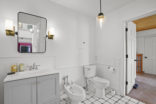 bathroom with vanity, tile patterned flooring, wainscoting, toilet, and a bidet