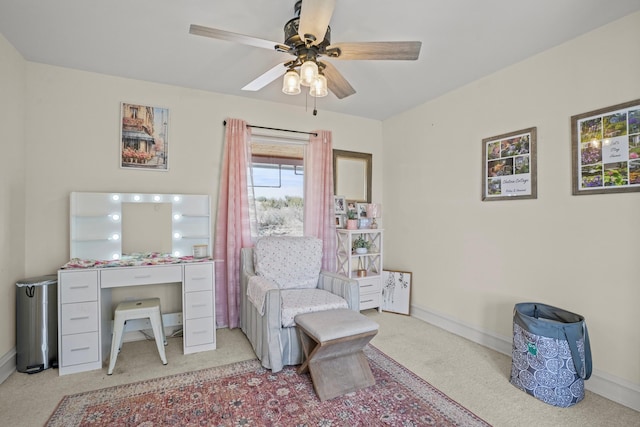 living area featuring baseboards, light carpet, and ceiling fan