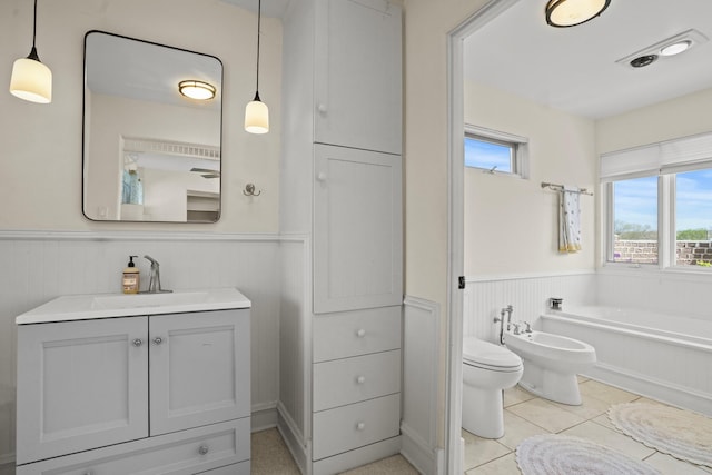 bathroom featuring vanity, tile patterned flooring, wainscoting, a bath, and a bidet