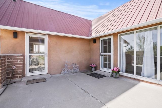view of exterior entry featuring a patio, metal roof, and stucco siding
