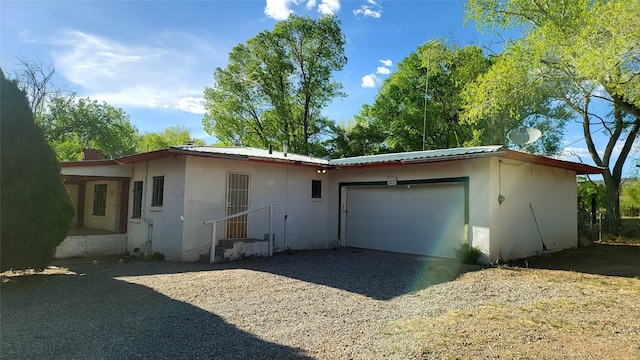 exterior space featuring an attached garage, stucco siding, gravel driveway, and metal roof