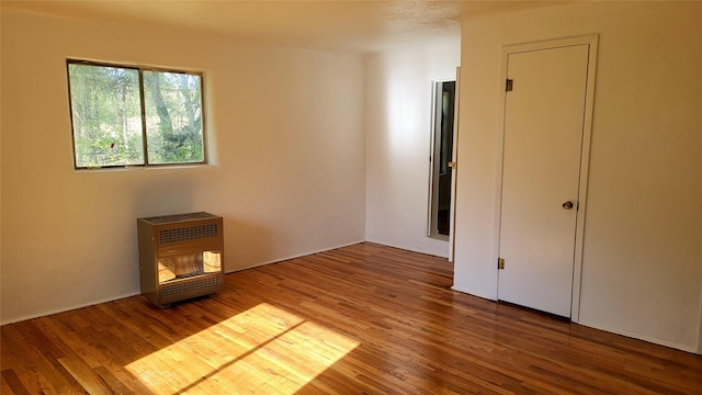 unfurnished bedroom with heating unit and wood finished floors