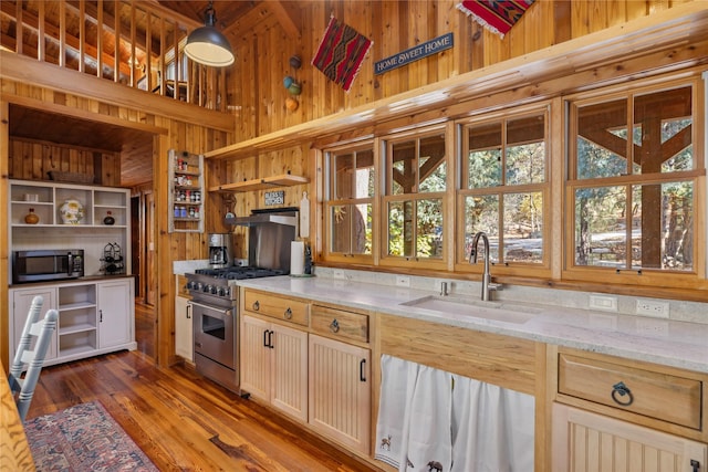 kitchen featuring open shelves, light stone countertops, wooden walls, a sink, and appliances with stainless steel finishes