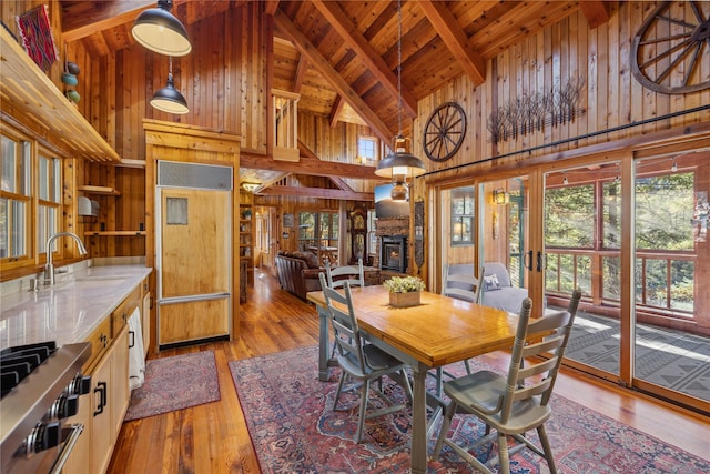 dining room featuring wood walls, beamed ceiling, high vaulted ceiling, wooden ceiling, and light wood finished floors