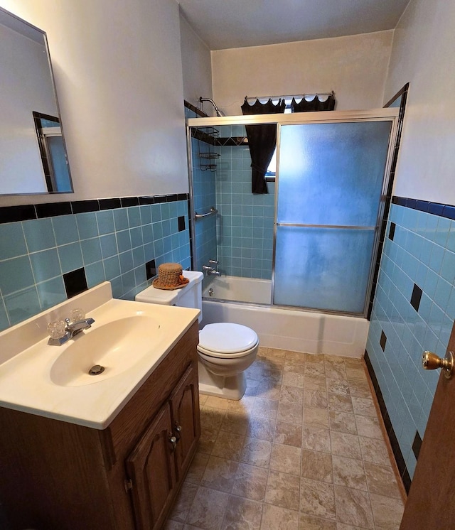 full bath with vanity, toilet, a wainscoted wall, tile walls, and bath / shower combo with glass door