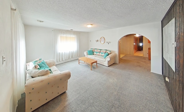 living area with carpet floors, arched walkways, and a textured ceiling