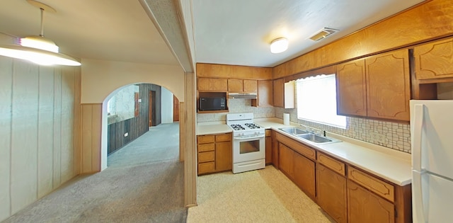 kitchen with arched walkways, under cabinet range hood, brown cabinets, and white appliances