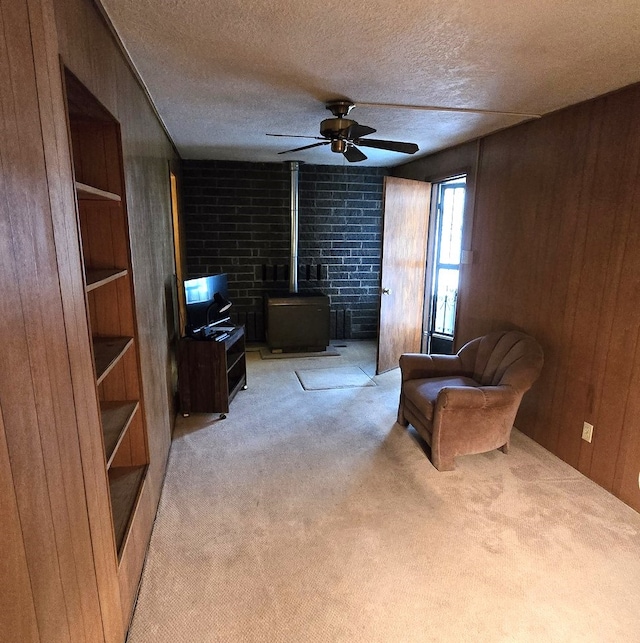 sitting room featuring light carpet, a wood stove, a textured ceiling, wood walls, and a ceiling fan