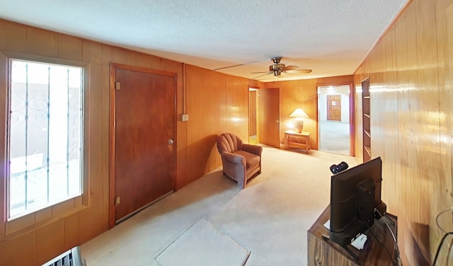 carpeted living area with a textured ceiling, wood walls, and ceiling fan