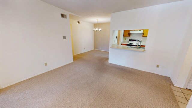 empty room featuring a sink, light carpet, a notable chandelier, and visible vents