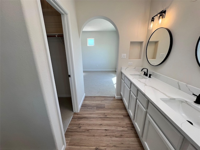 full bathroom with double vanity, baseboards, a sink, and wood finished floors