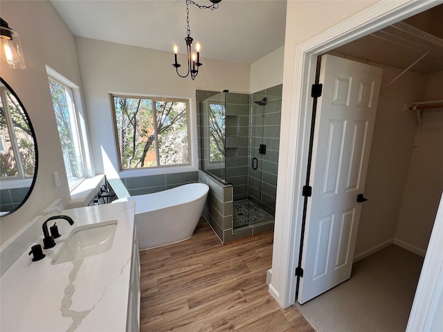bathroom with a freestanding bath, an inviting chandelier, a shower stall, wood finished floors, and a spacious closet