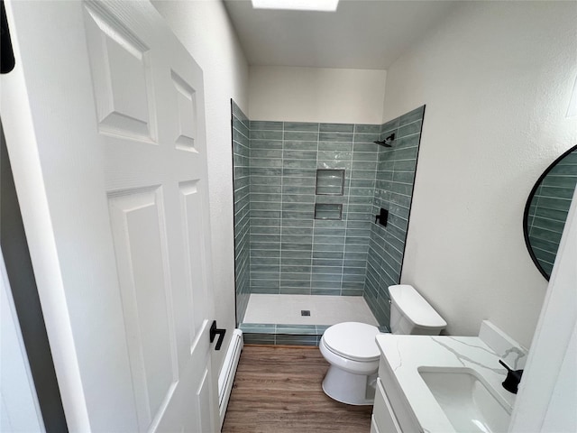 full bathroom featuring a tile shower, baseboard heating, vanity, toilet, and wood finished floors