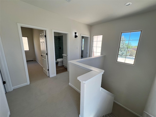 hallway featuring baseboards, an upstairs landing, baseboard heating, and light carpet