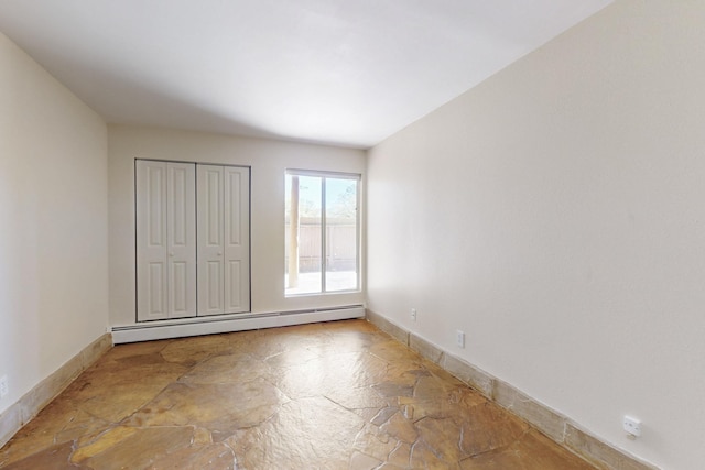 unfurnished bedroom featuring stone flooring, baseboards, and baseboard heating