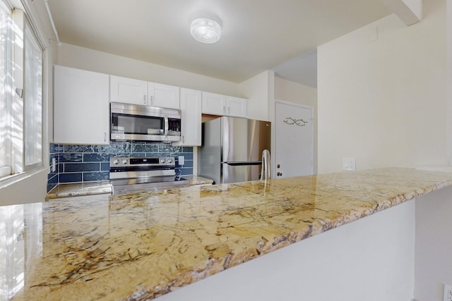 kitchen featuring decorative backsplash, a peninsula, white cabinetry, light stone counters, and appliances with stainless steel finishes