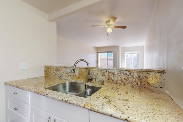 kitchen with a sink, white cabinets, light stone countertops, and ceiling fan